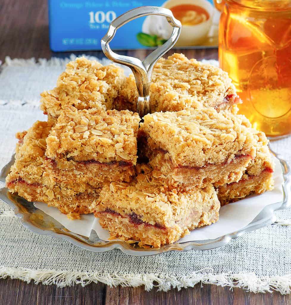 stacked cranberry oatmeal bars on an old-fashioned serving tray with a glass of iced tea in the background.