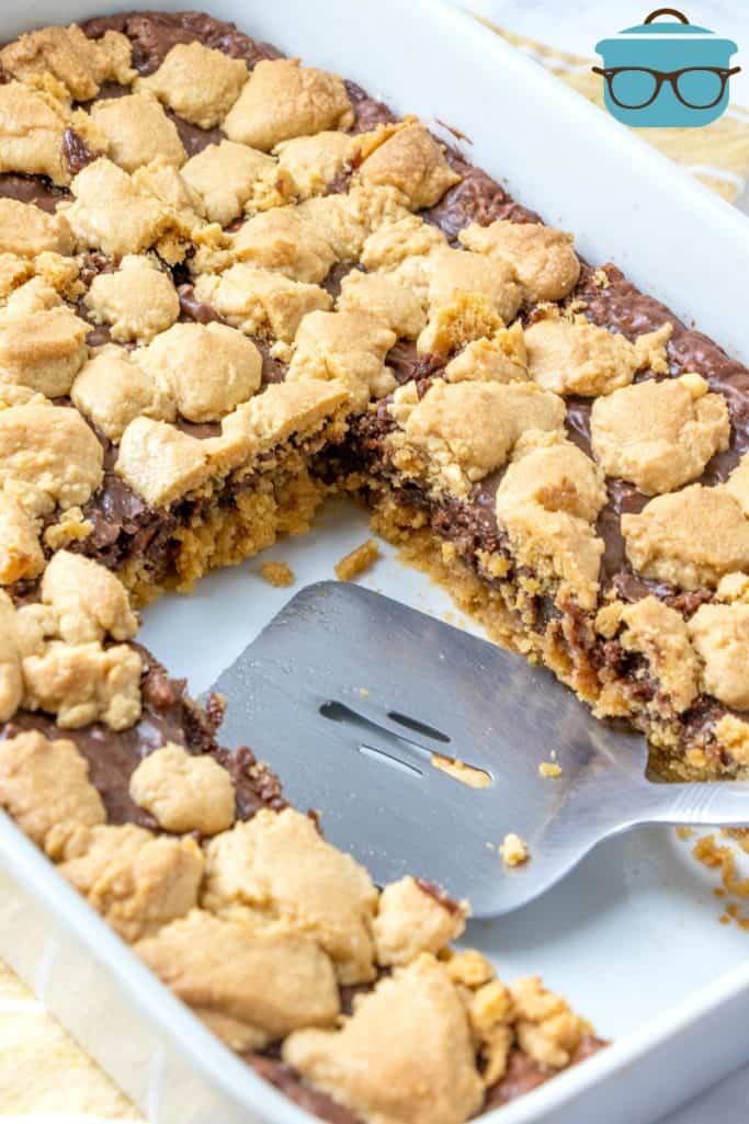 Fudge-filled Peanut Butter Bars in a baking dish, slices cut out and shown with a spatula