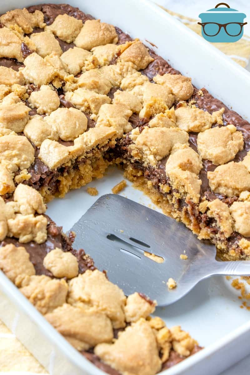 Fudge-filled Peanut Butter Bars in a baking dish, slices cut out and shown with a spatula.