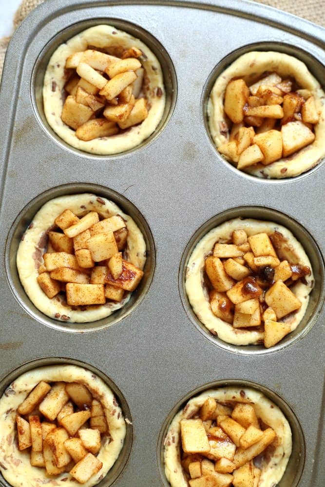 apple filling spooned into cinnamon rolls in a muffin tin