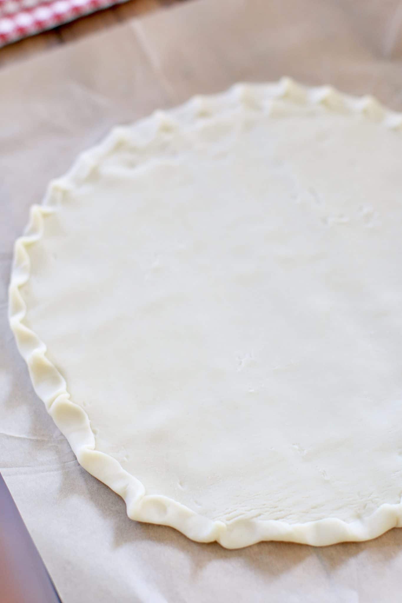 refrigerated pie crust placed on parchment and pressed into a circle with crimped edges.