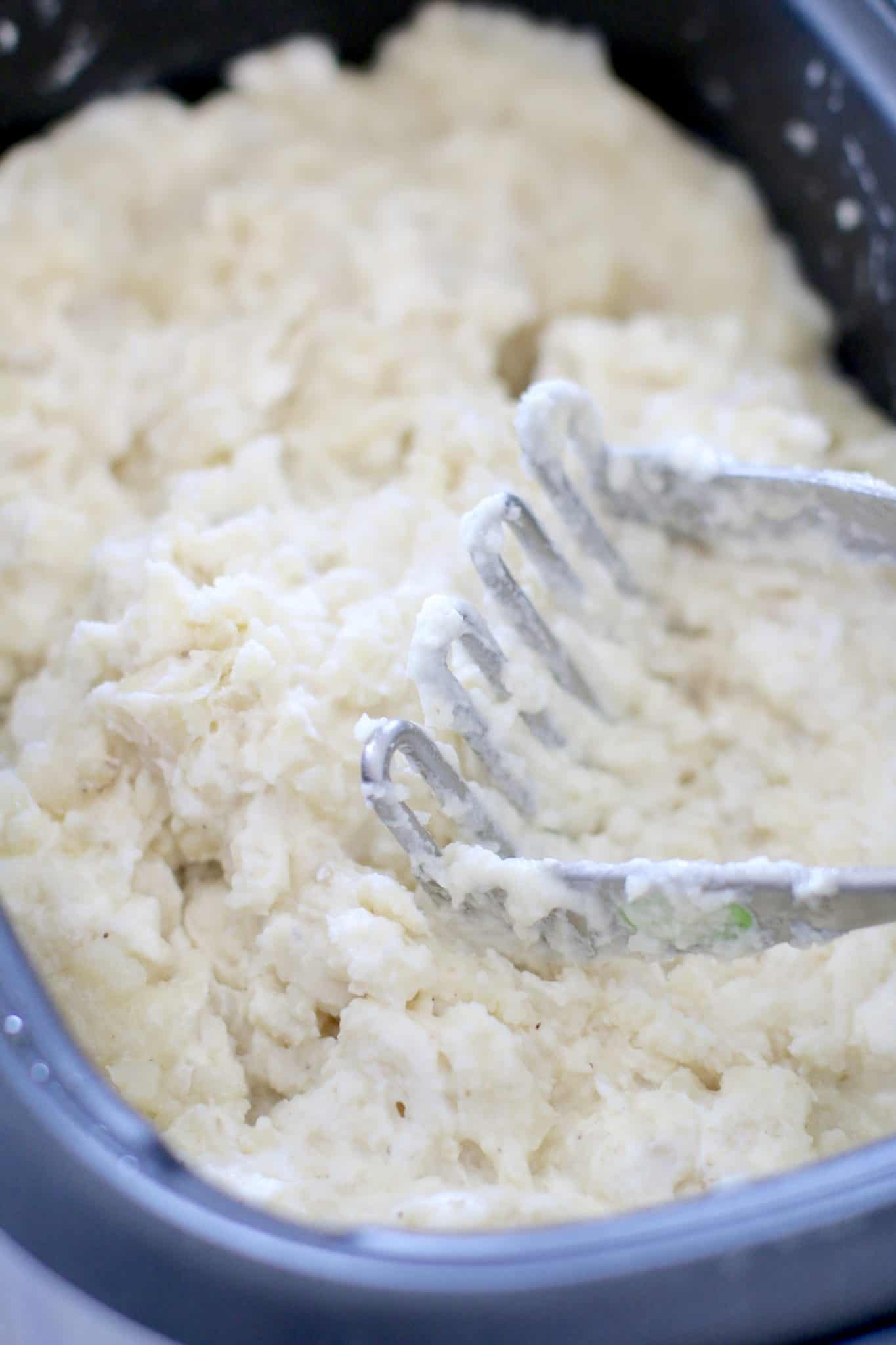 mashed potatoes in slow cooker with a potato masher.