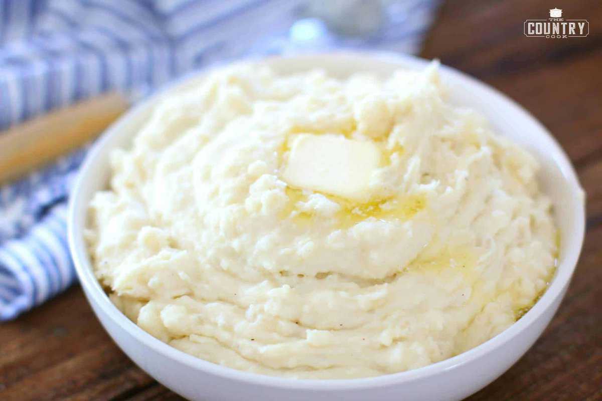 slow cooker mashed potatoes shown in a white bowl with melted butter on top of the mashed potatoes.