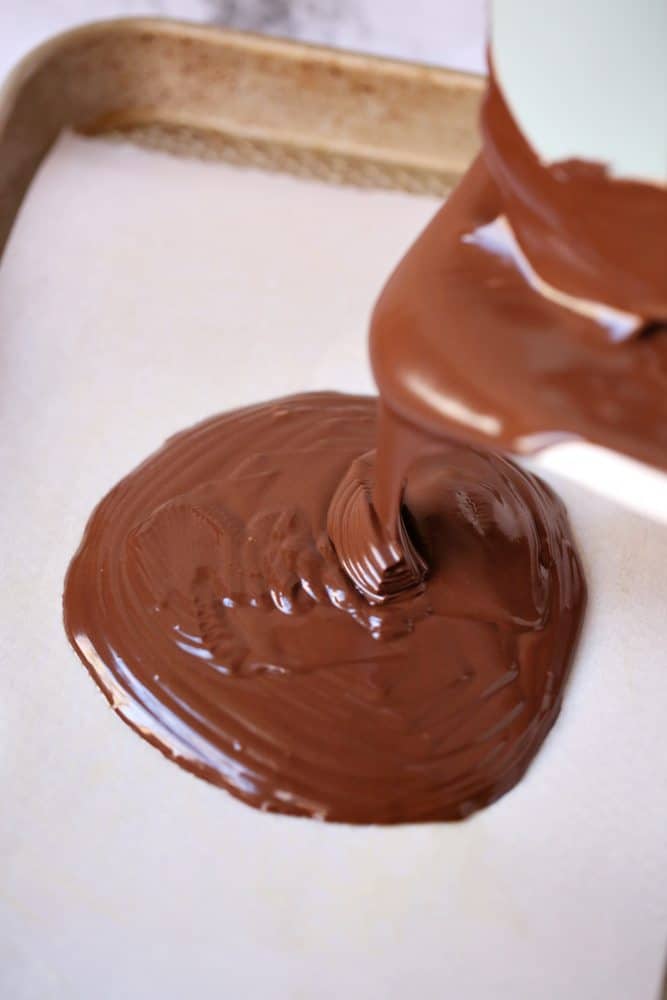 pouring melted chocolate almond bark onto a parchment paper lined baking sheet. 