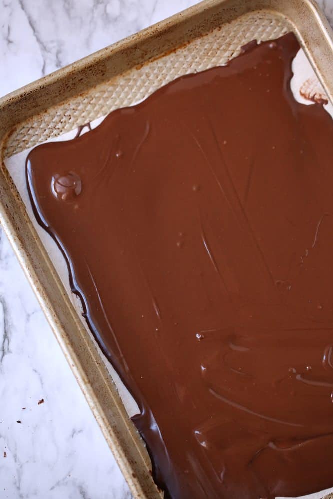 melted chocolate almond bark shown on a white parchment paper lined baking sheet. 