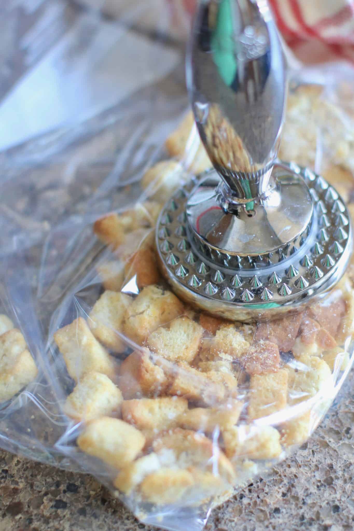 garlic croutons in a plastic bag being crushed by a meat mallet. 