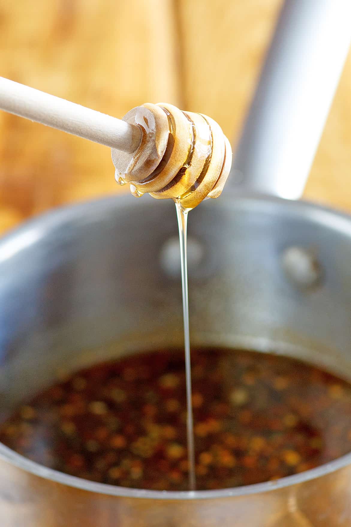 honey garlic glaze for chicken in a sauce pan with honey dipper shown over pot.