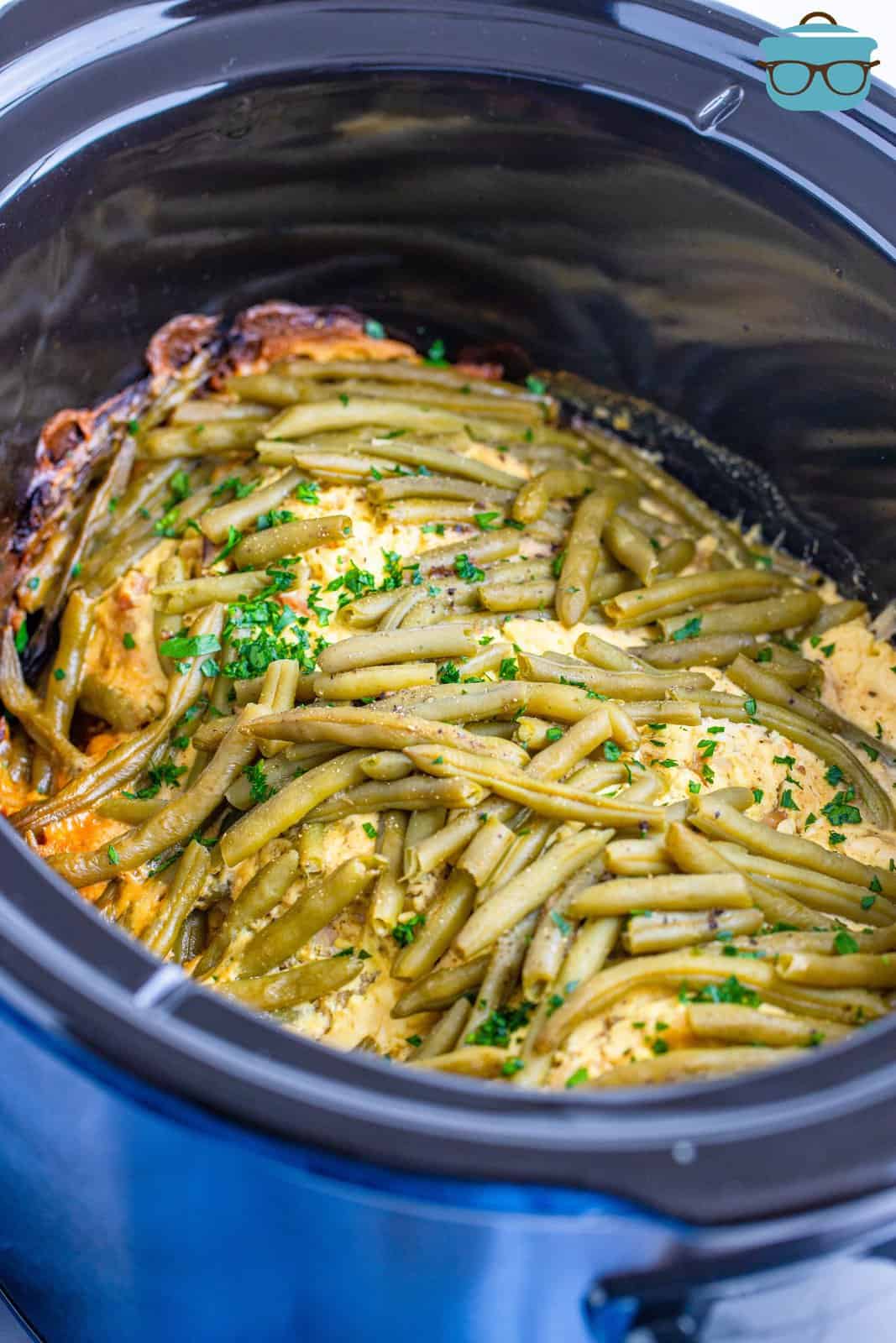 fully cooked chicken, stuffing and green beans shown in an oval crock pot.