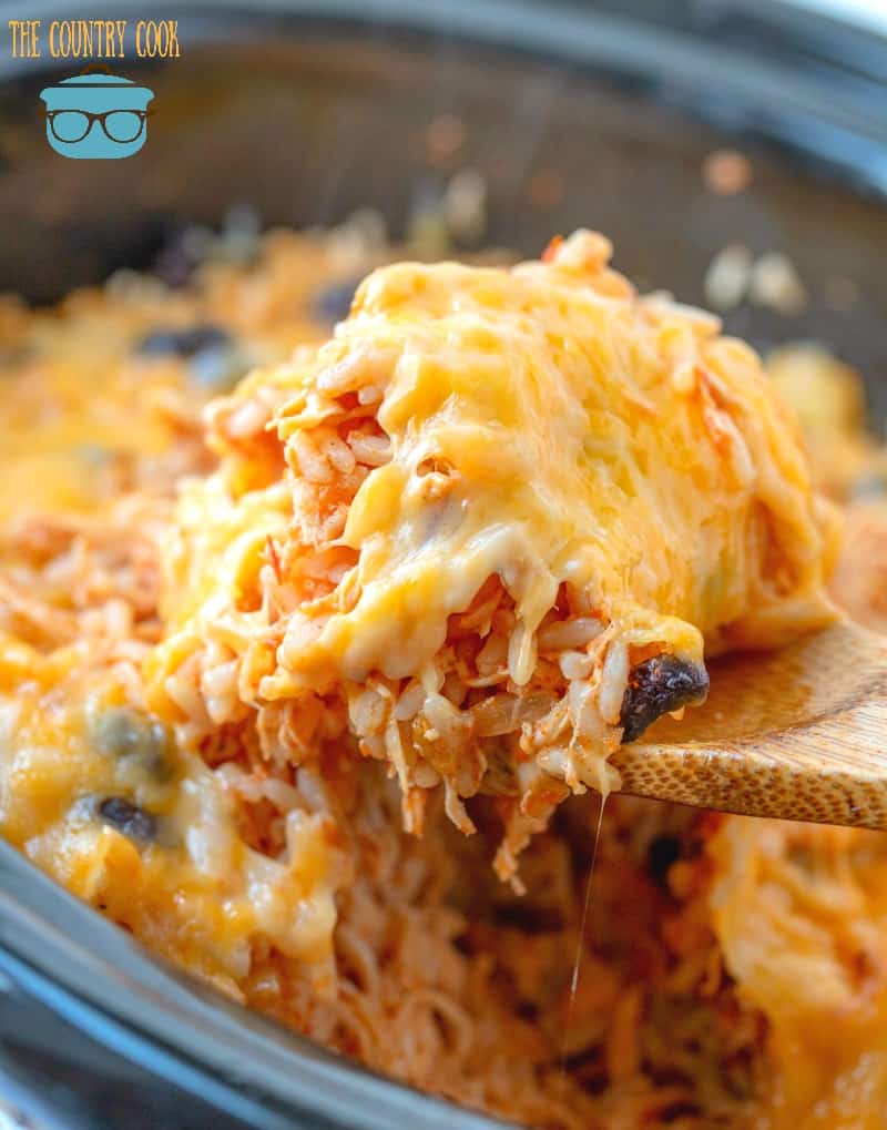Crock Pot Chicken and Rice topped with melted cheese being scooped up by a wooden spoon.