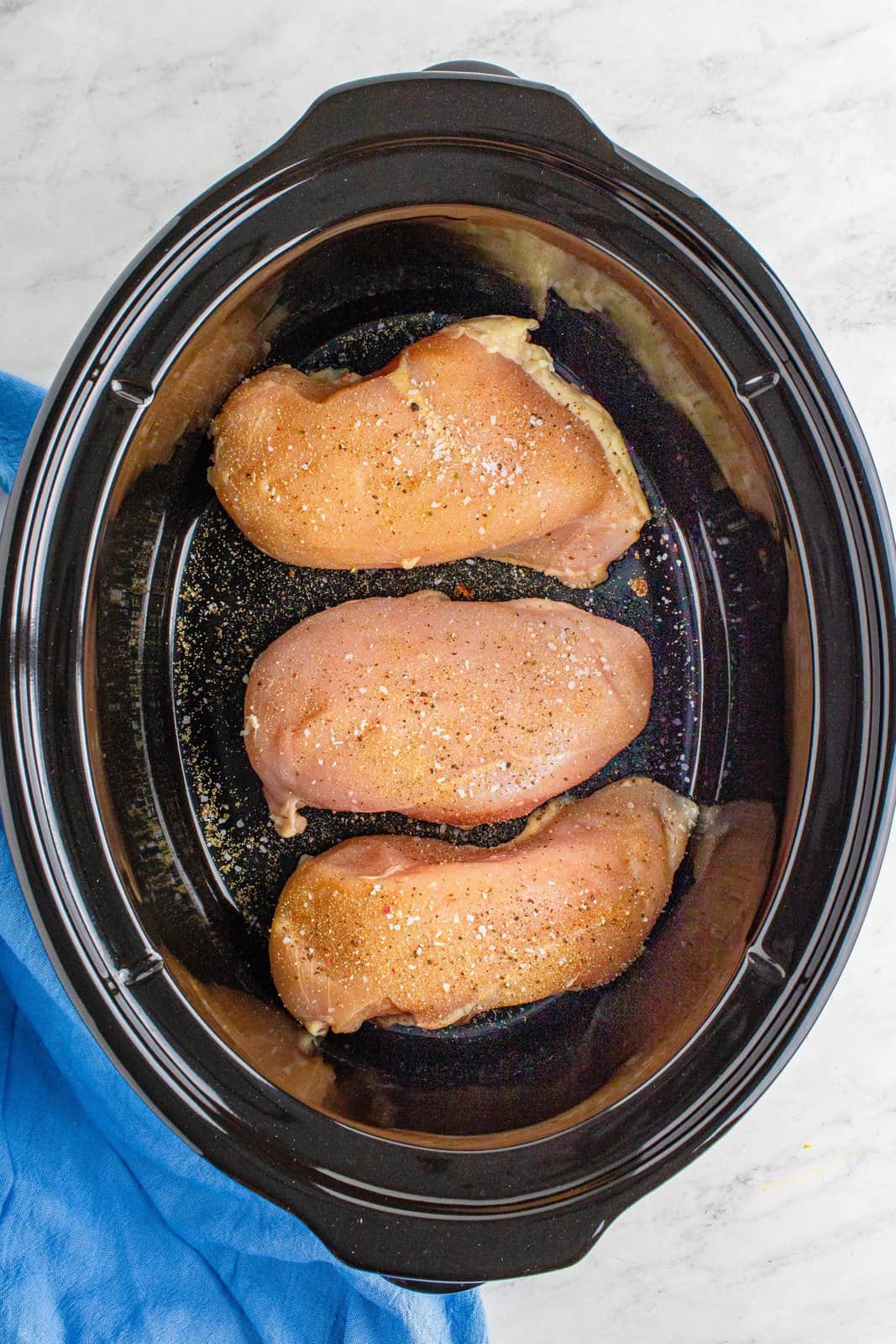 chicken breasts lined up in the bottom of an oval slow cooker.