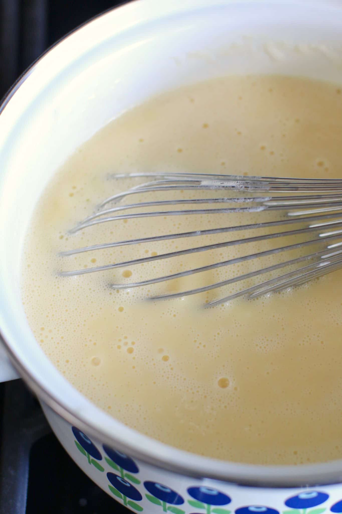 cooked custard shown in a saucepan with a whisk. 