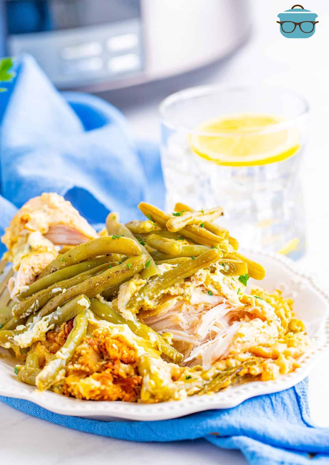chicken, stuffing and green beans shown served on a round white plate with a glass of ice water in the background.
