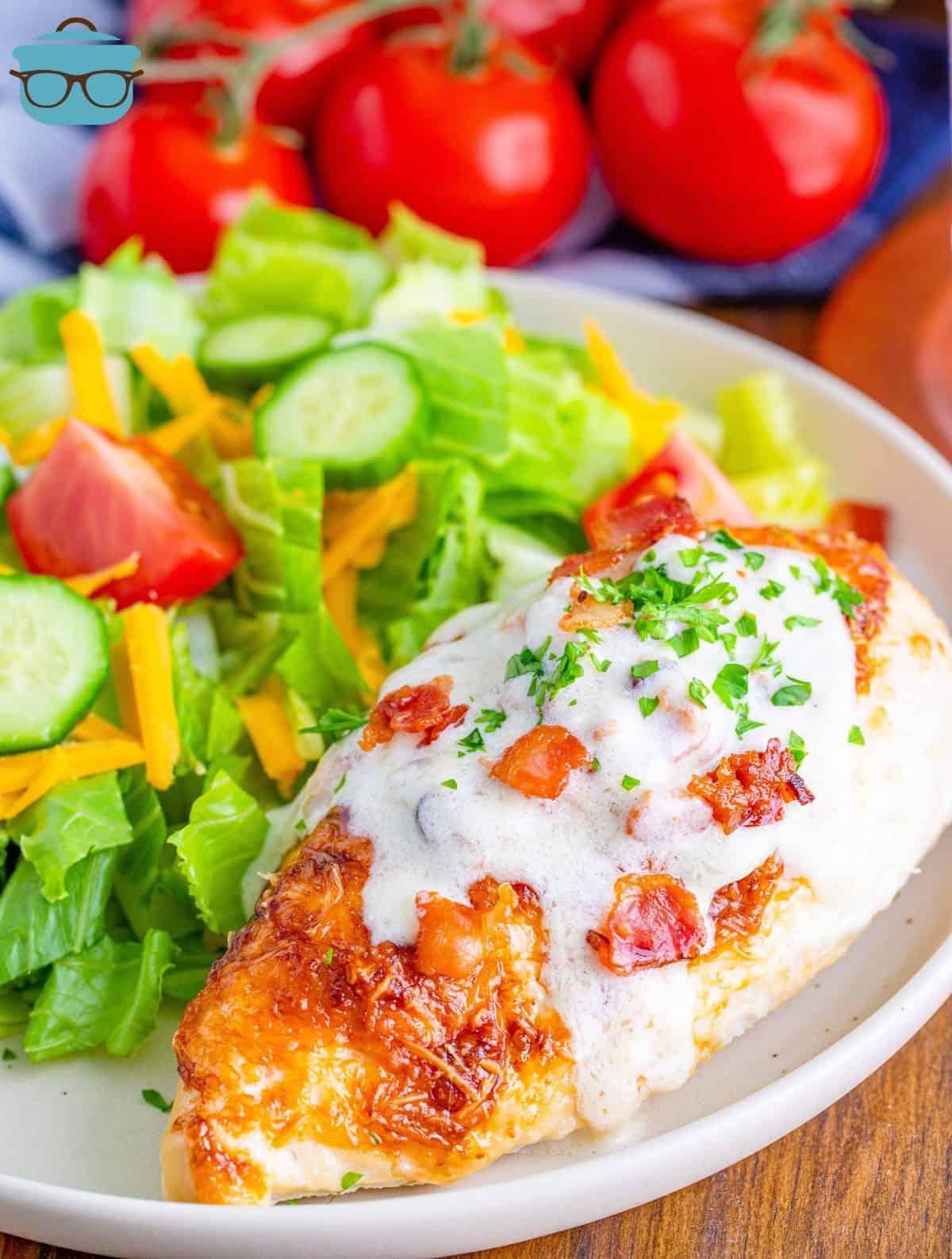 chicken breast on a plate with creamy bacon sauce poured on top with a salad on the side of the plate. 