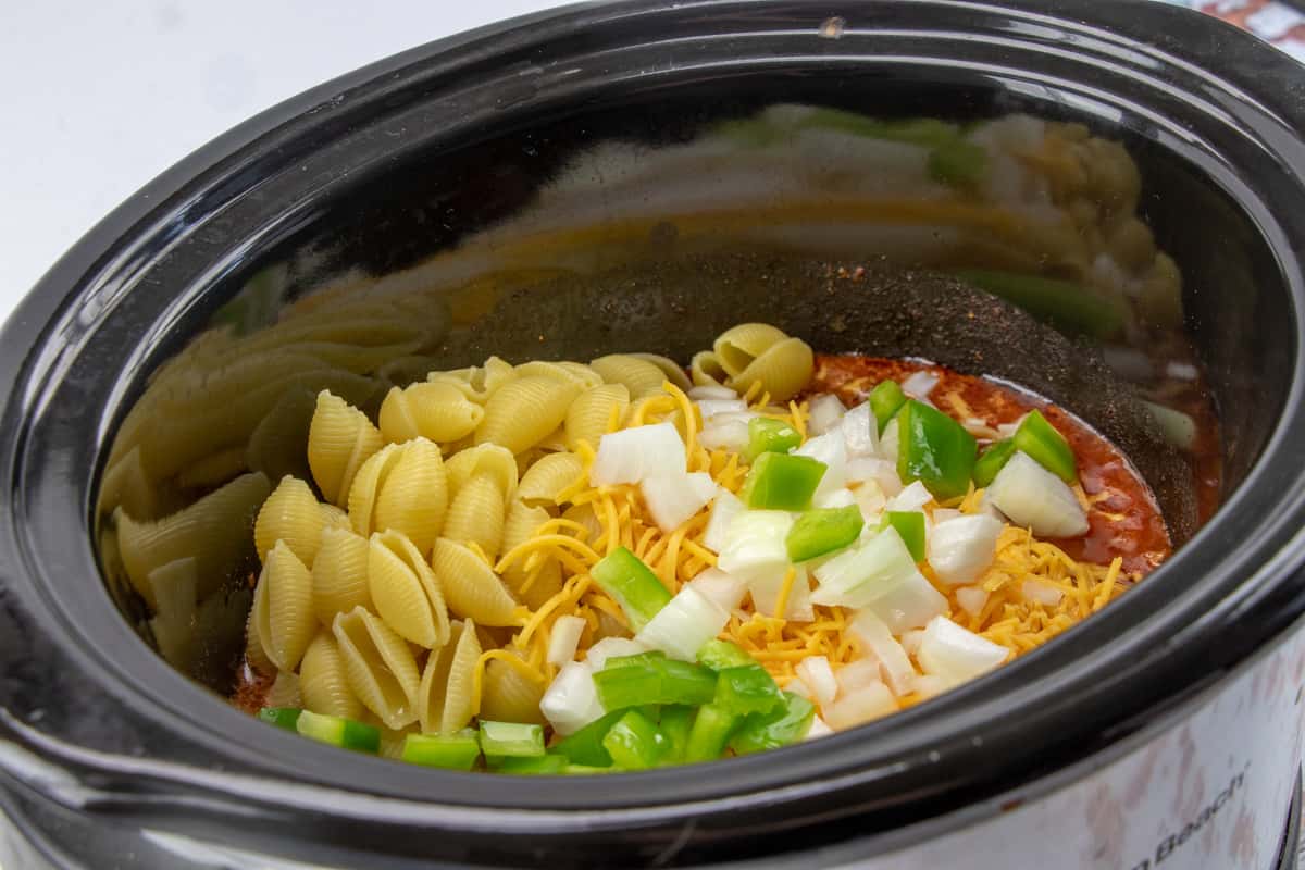 pasta shells, green pepper and onions added to ground beef, diced tomatoes and taco seasoning in an oval slow cooker.