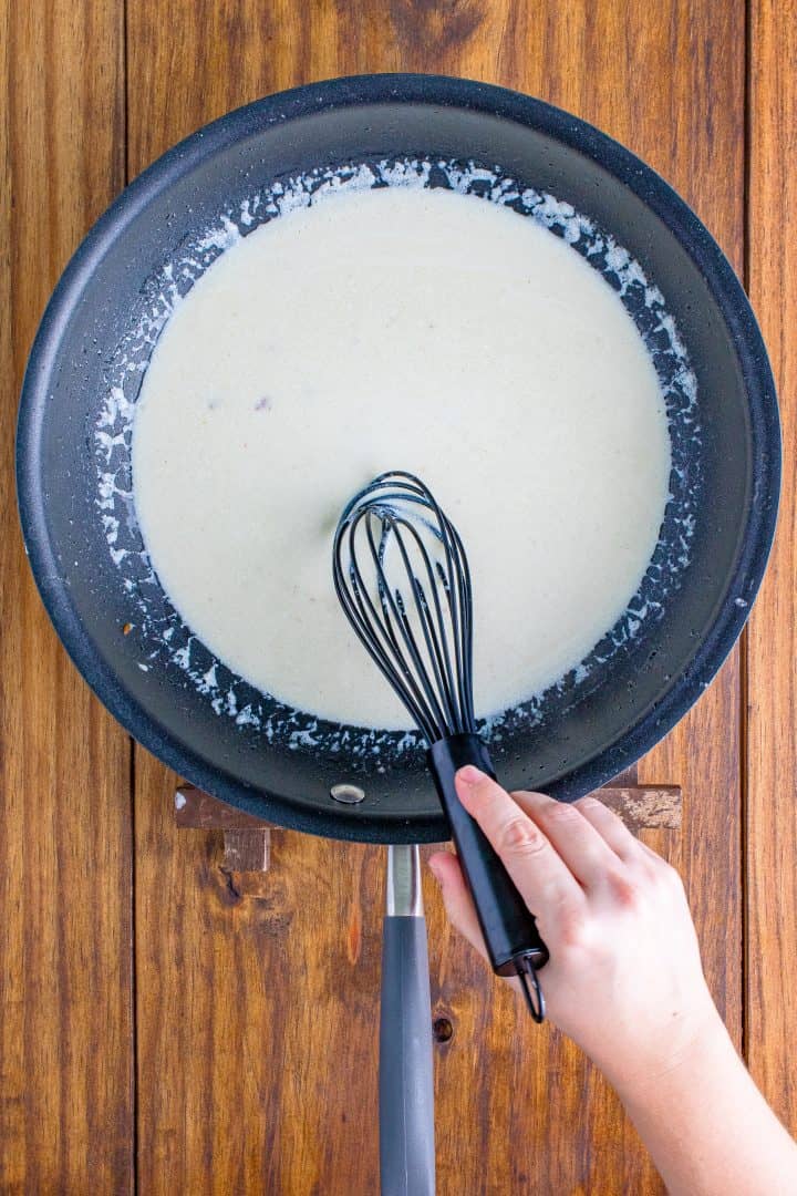 heavy cream added to pan and being stirred by a whisk.