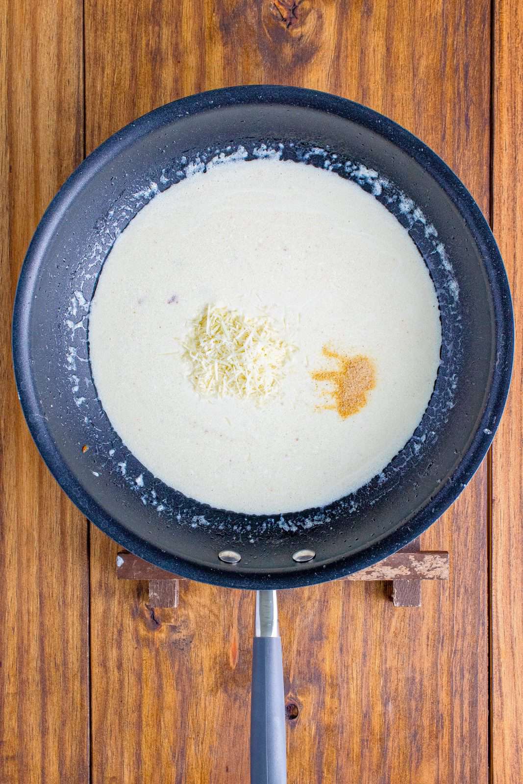 garlic powder and Parmesan cheese added to cream mixture in a skillet. 