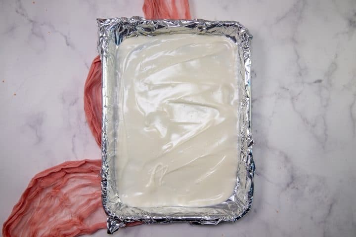 melted vanilla almond bark spread out on top of aluminum foil in a baking sheet.