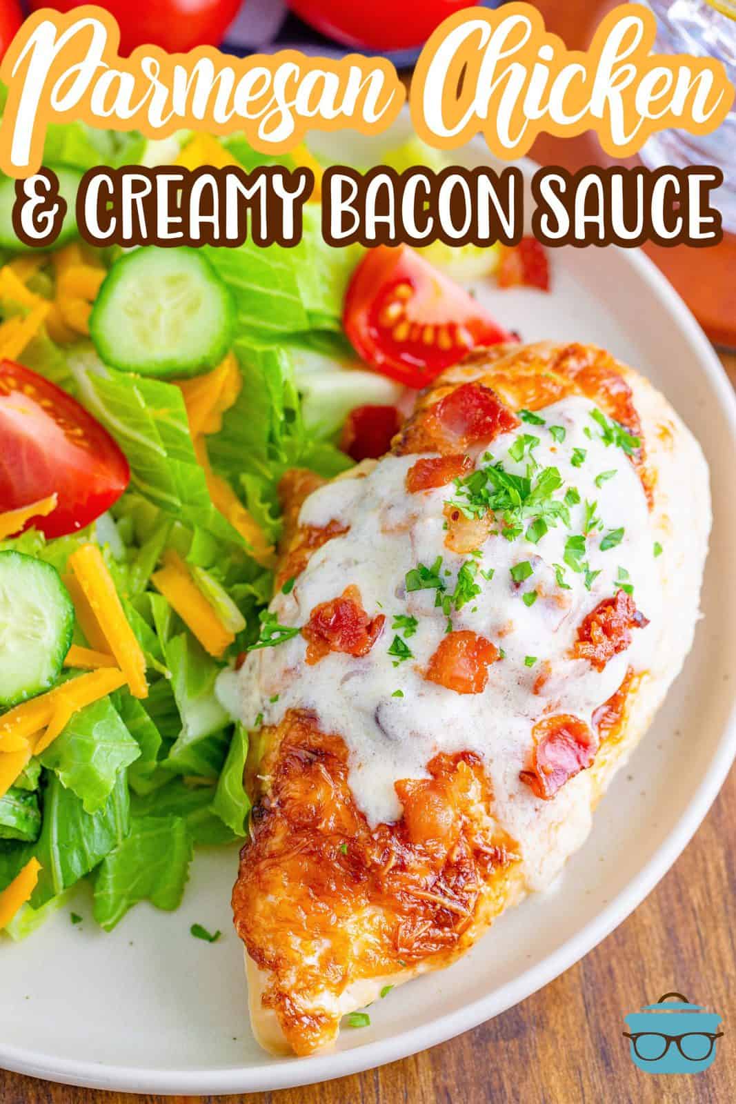 Bacon Parmesan Sauce on top of a Parmesan Chicken breast on a round white plate with a salad on the side. 