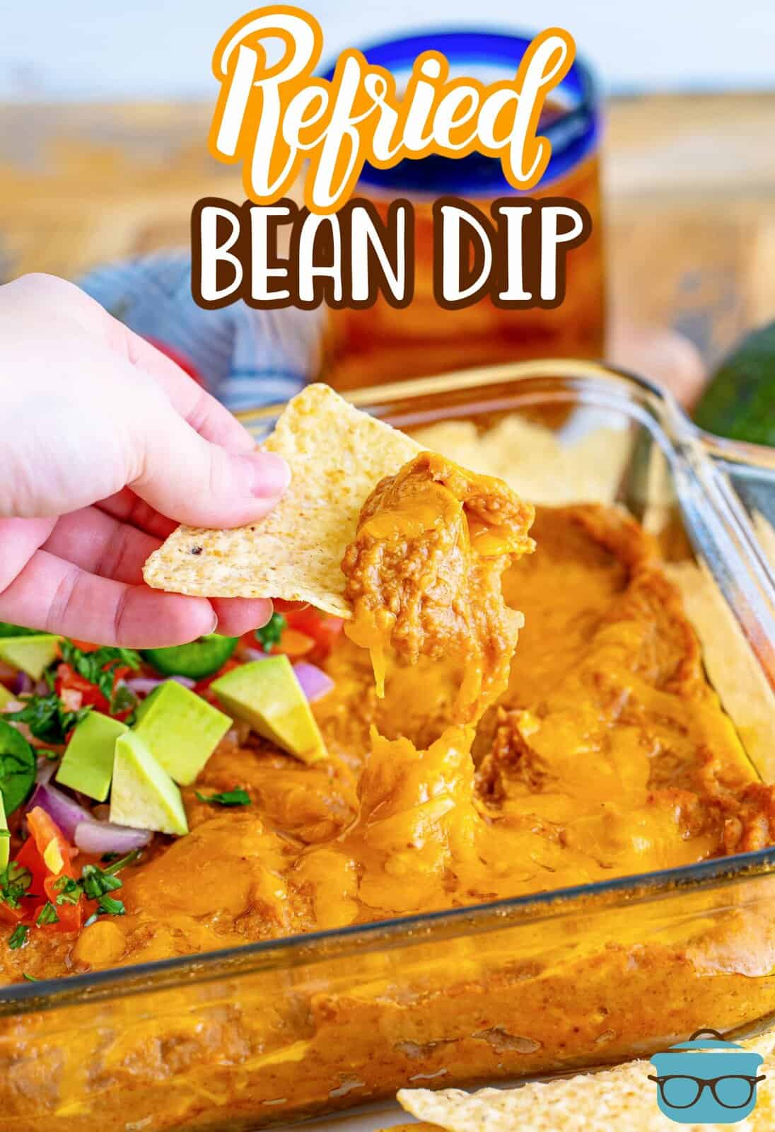 a hand holding up a tortilla chip with refried bean dip on it. 