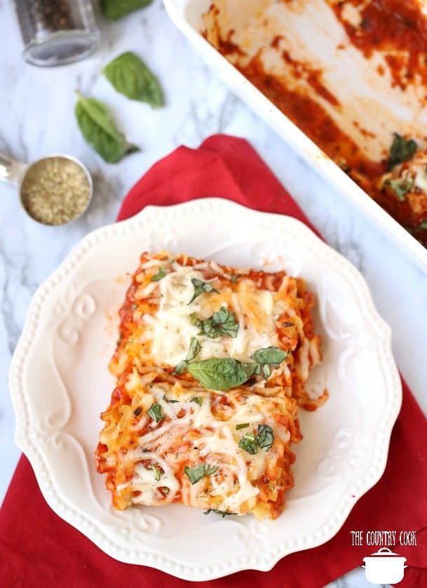 Easy Meatless Lasagna Rollups on a white plate with fresh basil and a baking dish in the background.