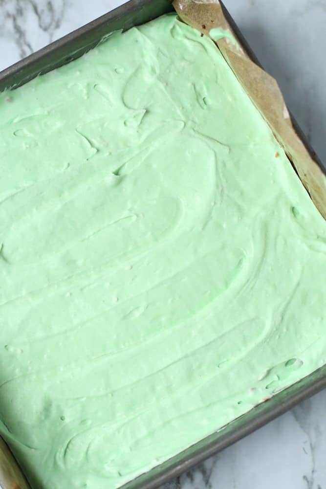 green-colored cheesecake batter spread on top of chocolate cheesecake layer