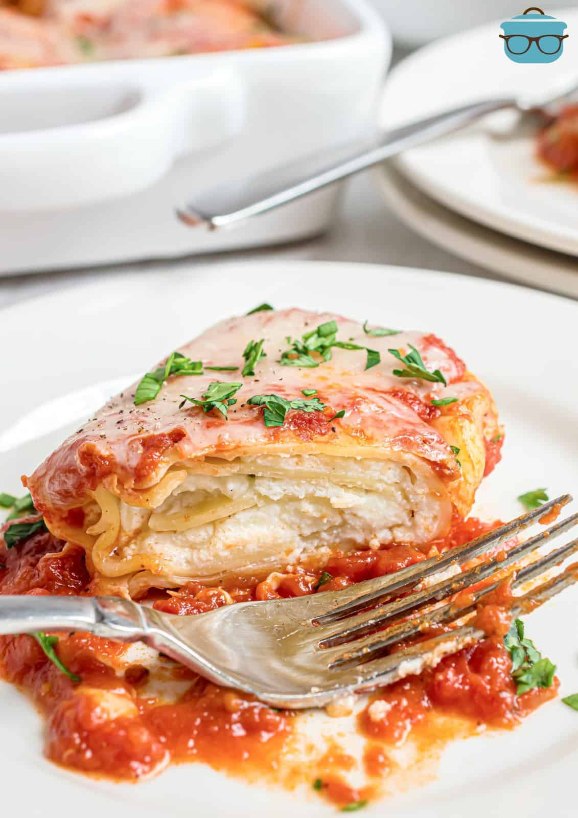 one lasagna rollup on a white plate with a bite taken out with a fork.