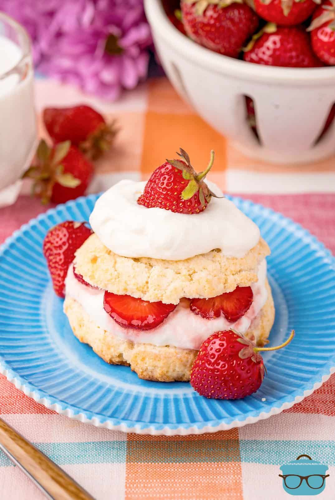 strawberry shortcake cut in half with whipped cream and strawberries layered in the middle all set on a blue plate.