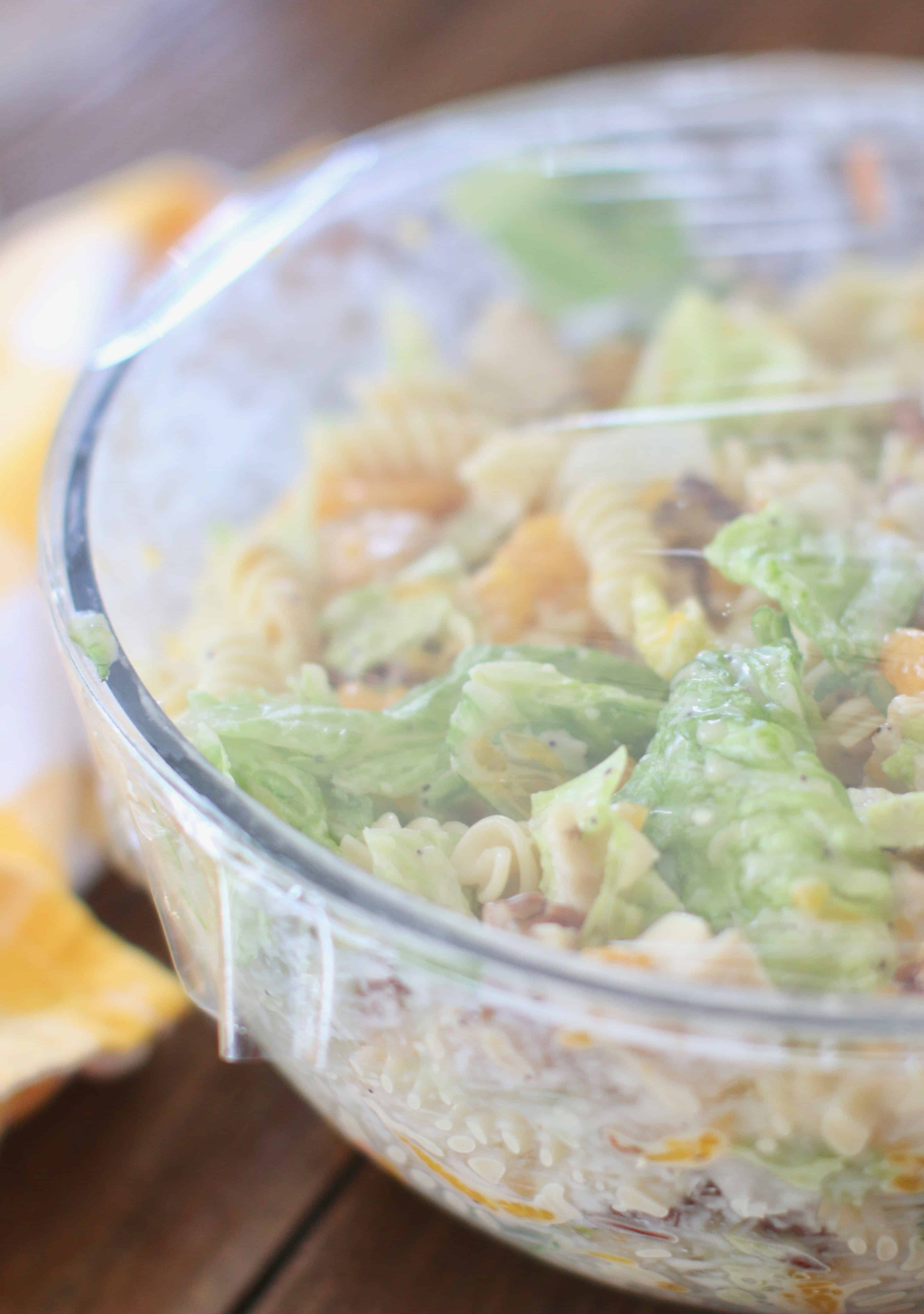 plastic wrap covered bowl with pasta, grilled chicken, lettuce, pecans and mandarin oranges.