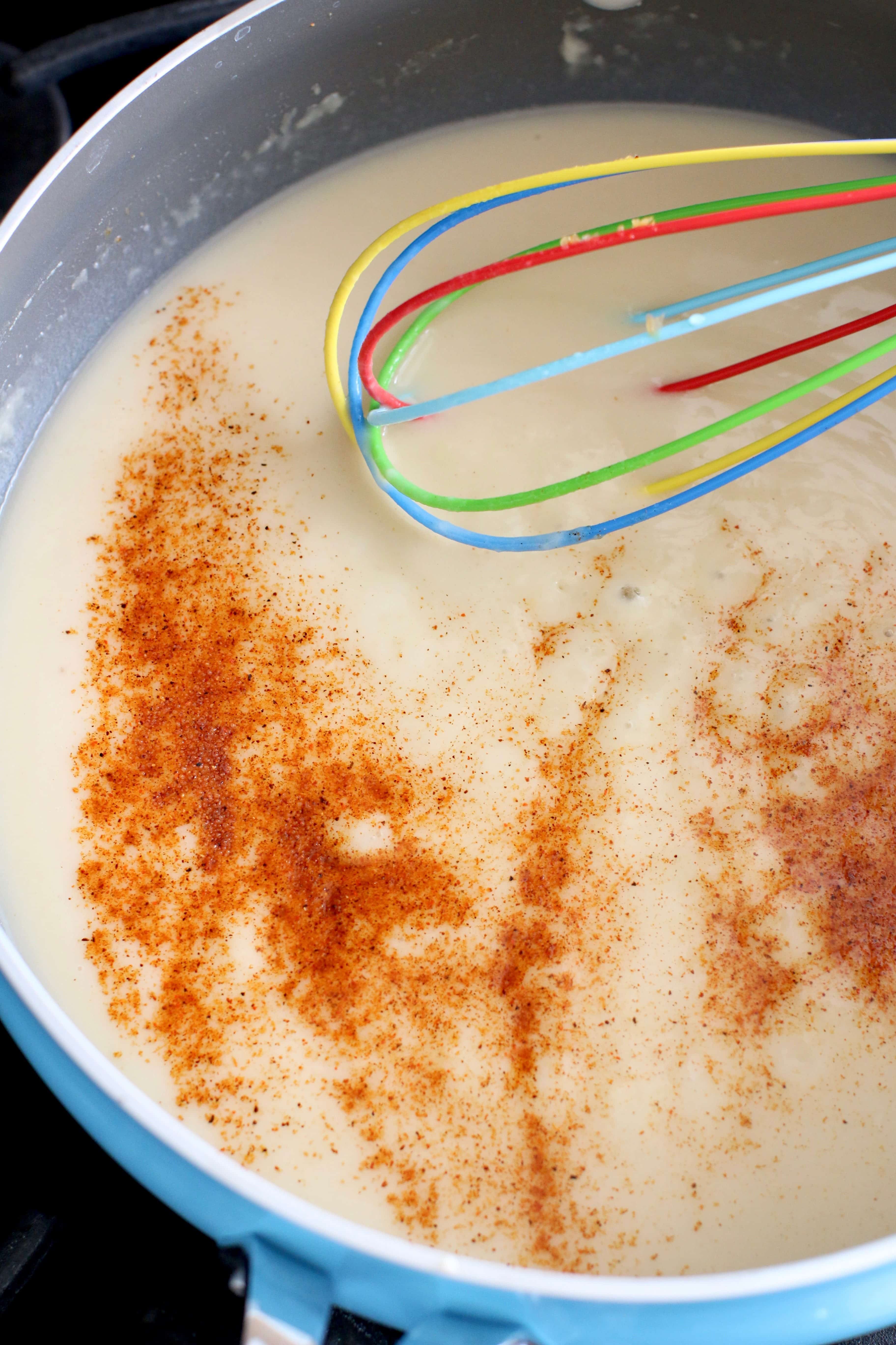 creole seasoning sprinkled into roux in a skillet with a whisk.