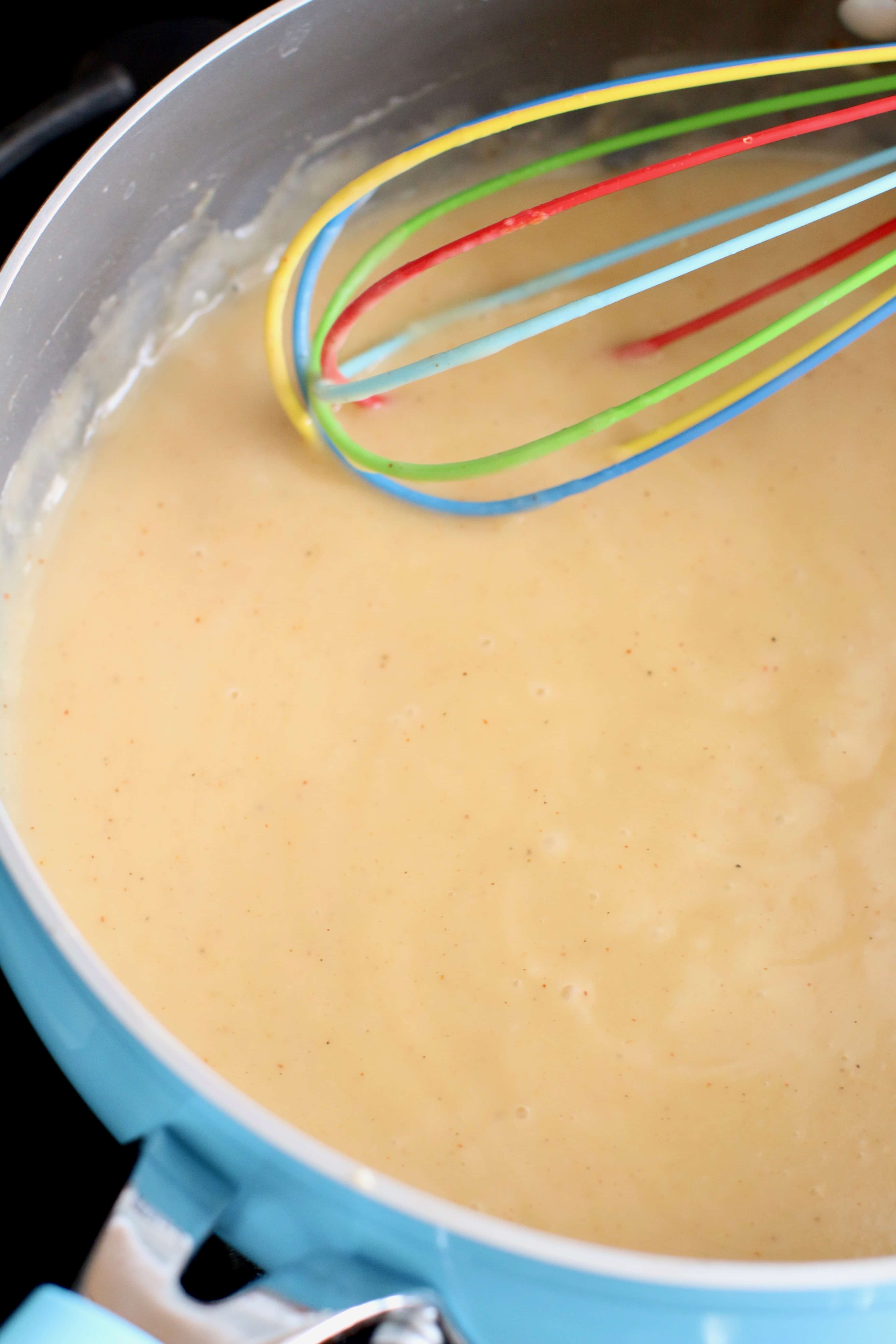 creamy sauce made with a roux and being whisked in a large skillet. 
