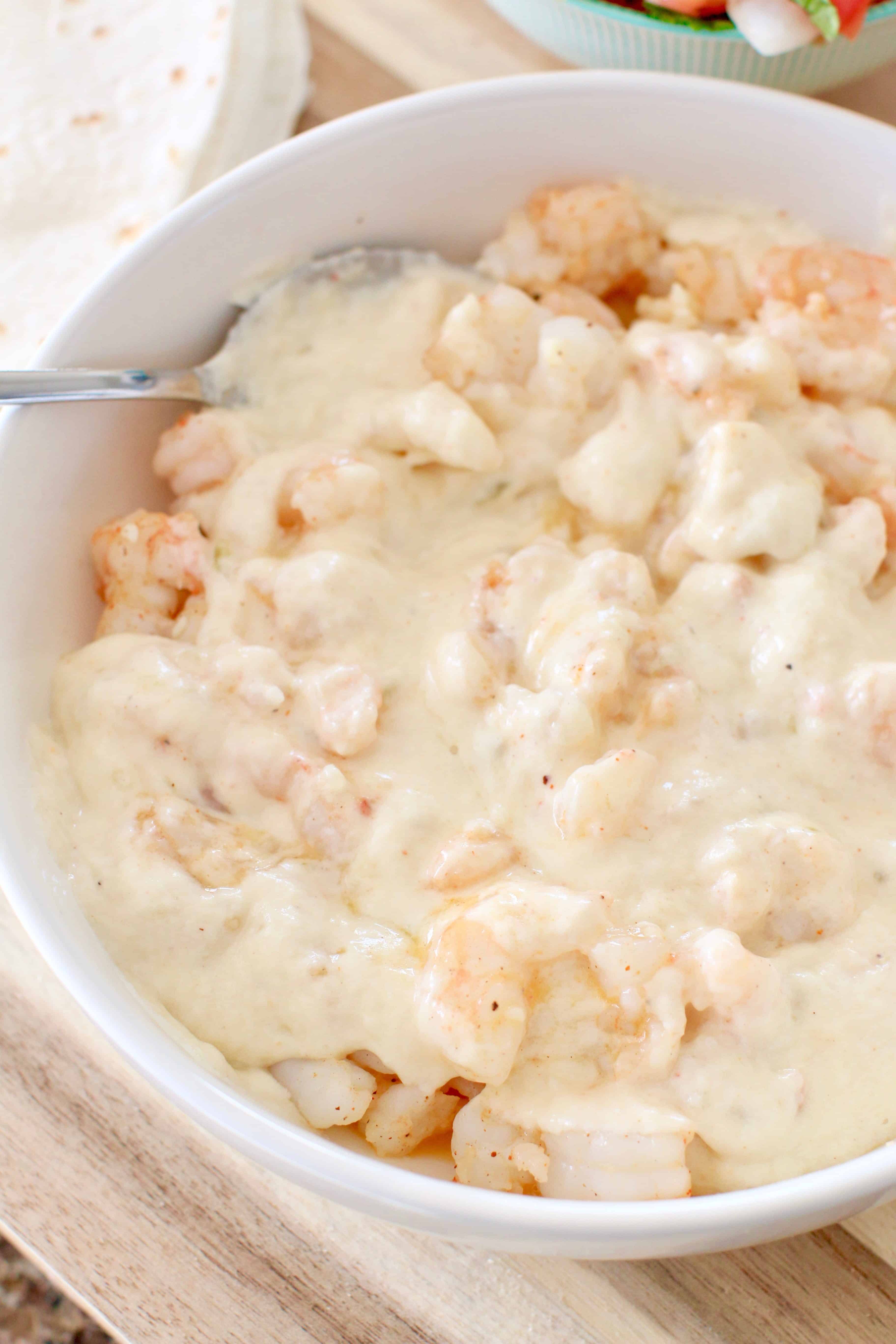 cheese sauce added to cooked shrimp in a white bowl.