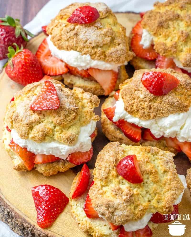 Strawberry Shortcakes with whipped cream and sweetened strawberries on a wooden board.