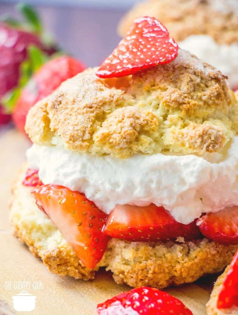 Layers of homemade shortcake with whipped cream and sweetened strawberries shown close up.