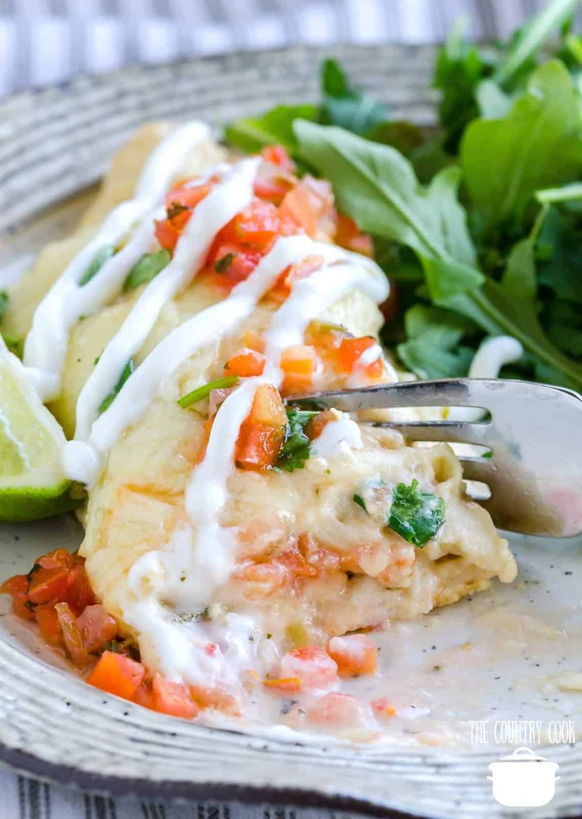 a fork slicing into a shrimp enchilada on a plate.