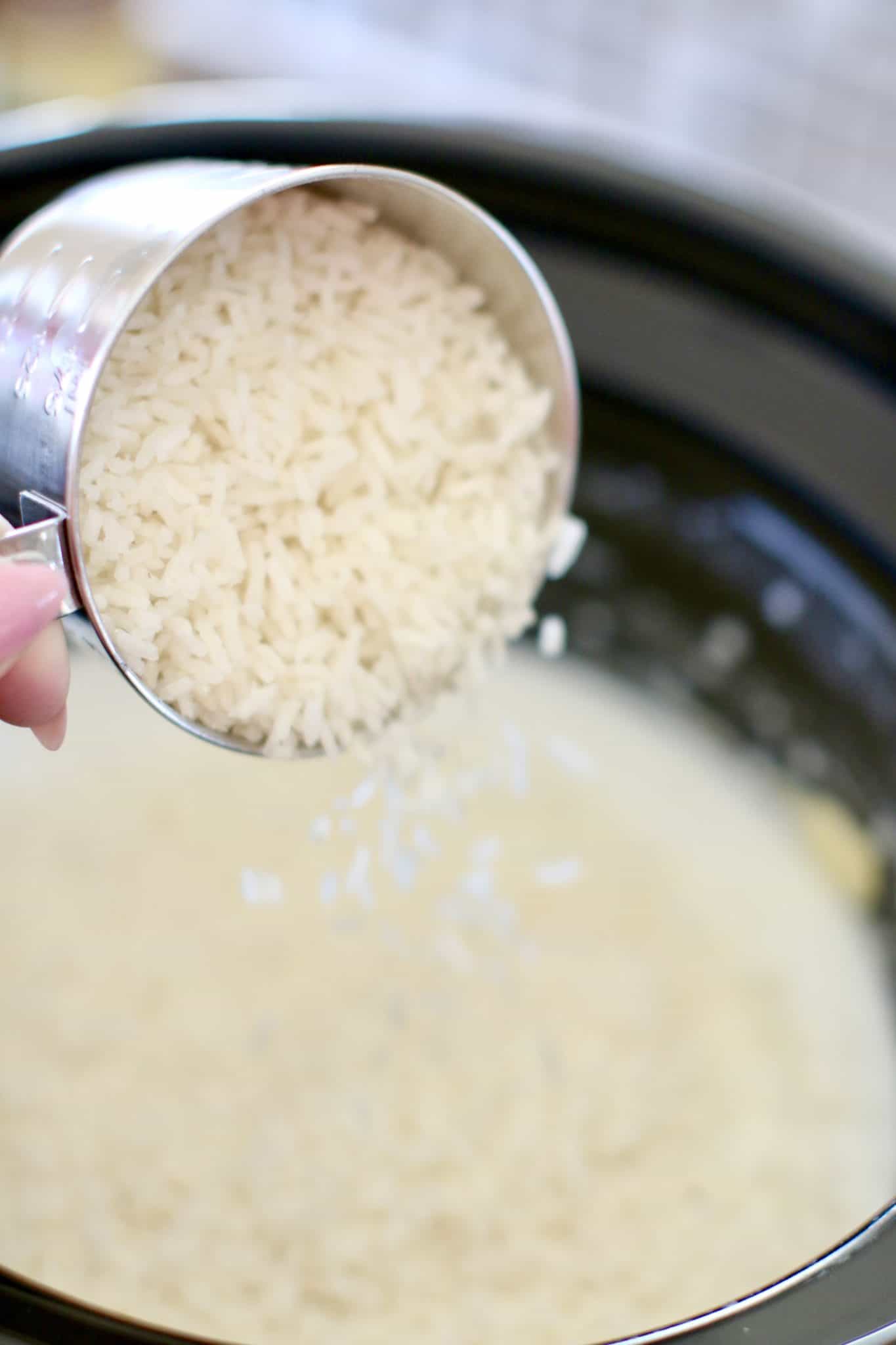 pouring white rice into milk and cream of coconut in slow cooker.