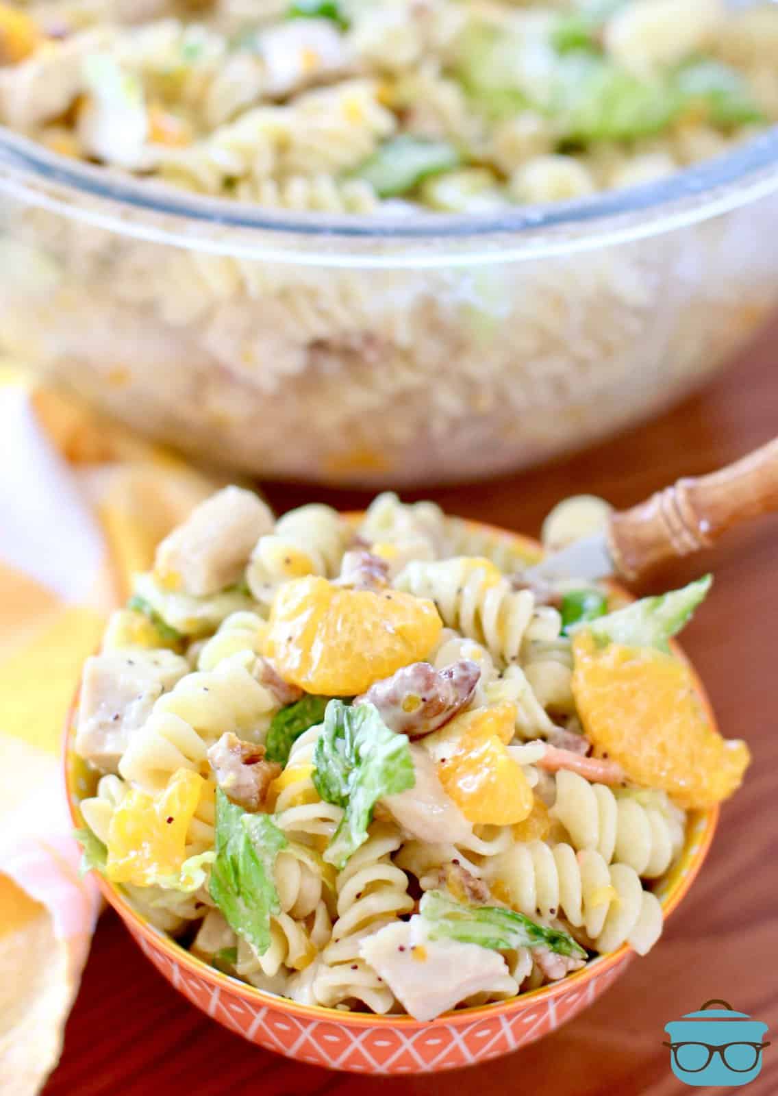 orange bowl filled with orange chicken pasta salad with a fork inserted into salad. 
