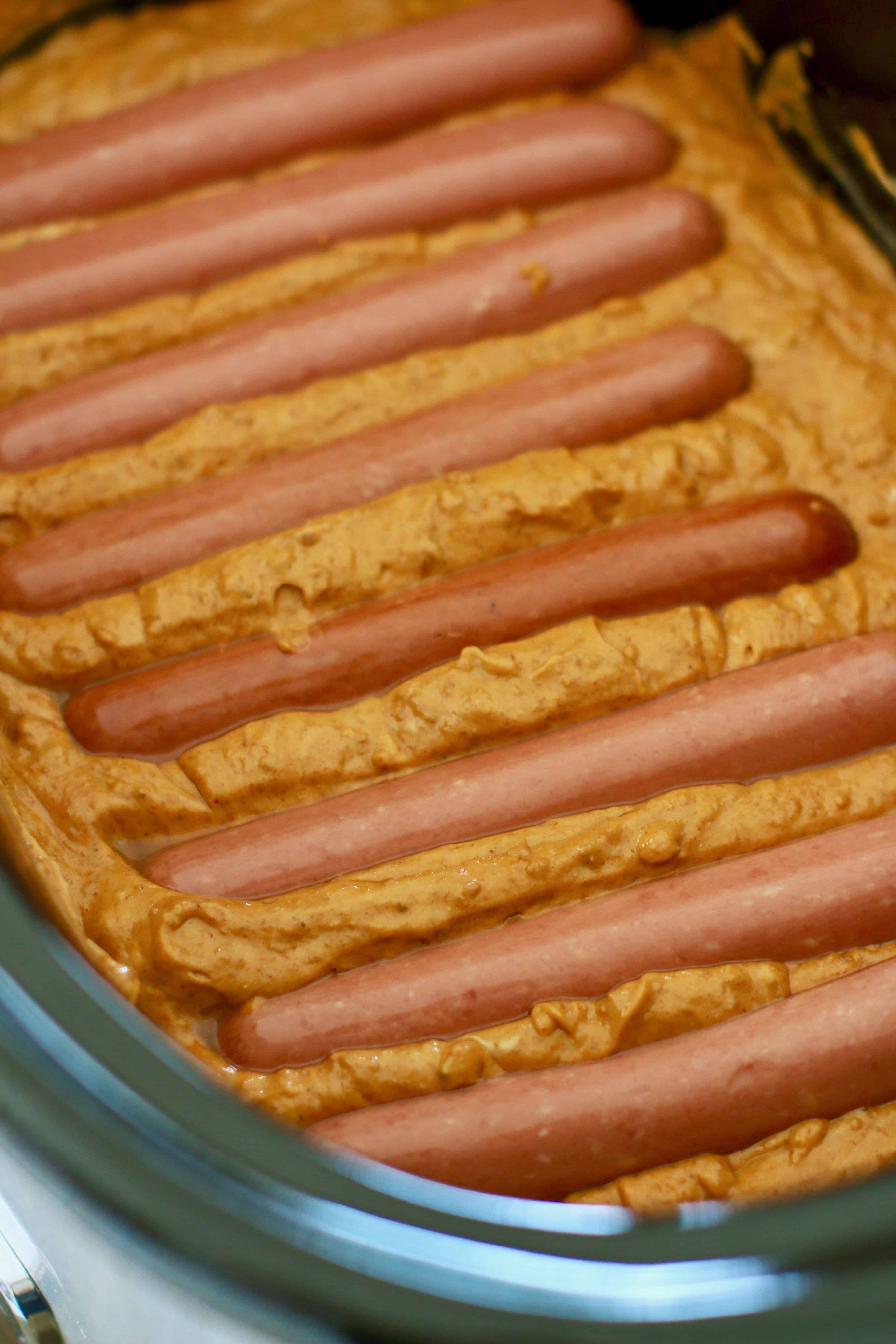 hot dogs in a row, laying on top of chili and cheese sauce.