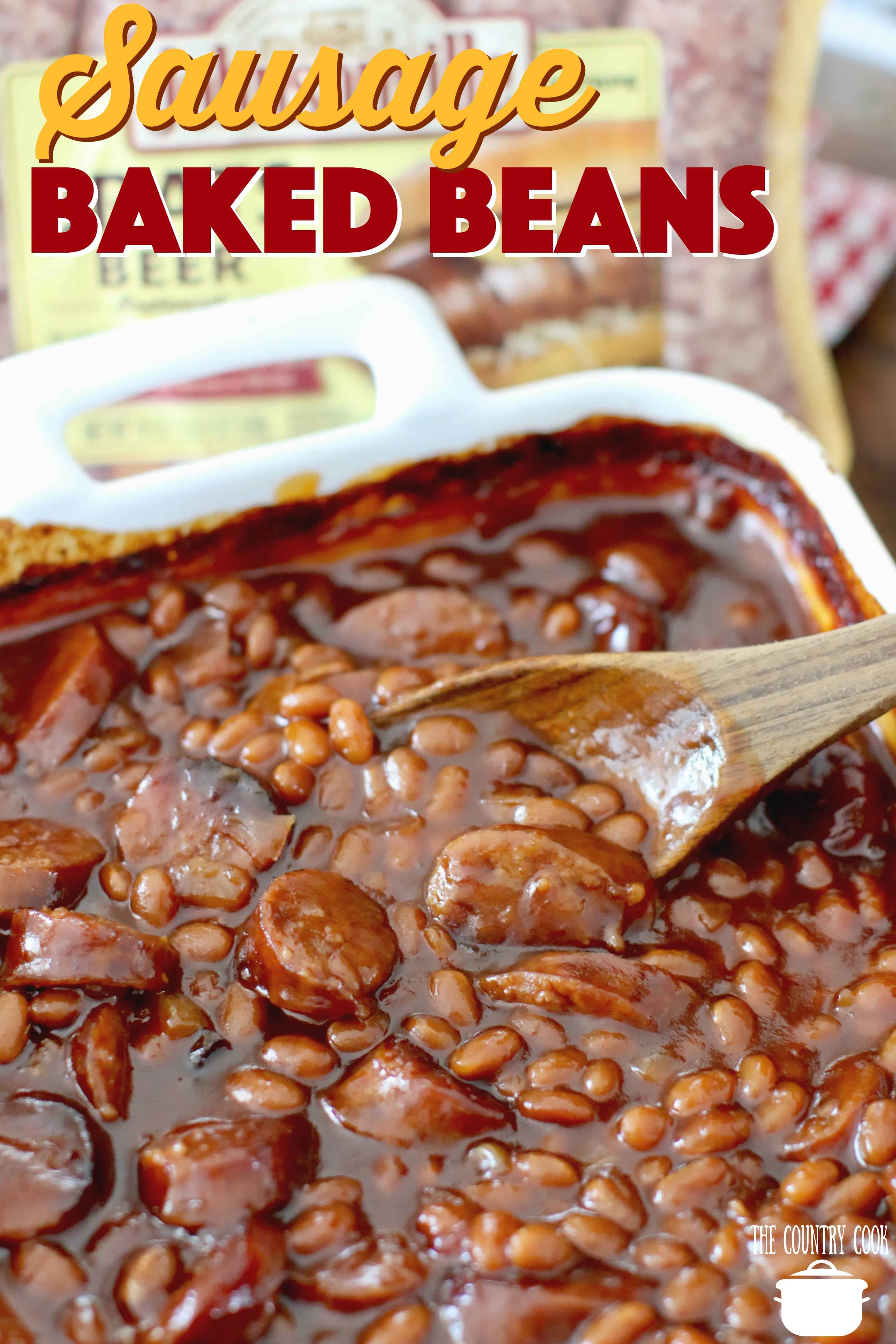 overhead photo of sausage baked beans in a white baking dish with a wooden spoon inserted into the beans. 