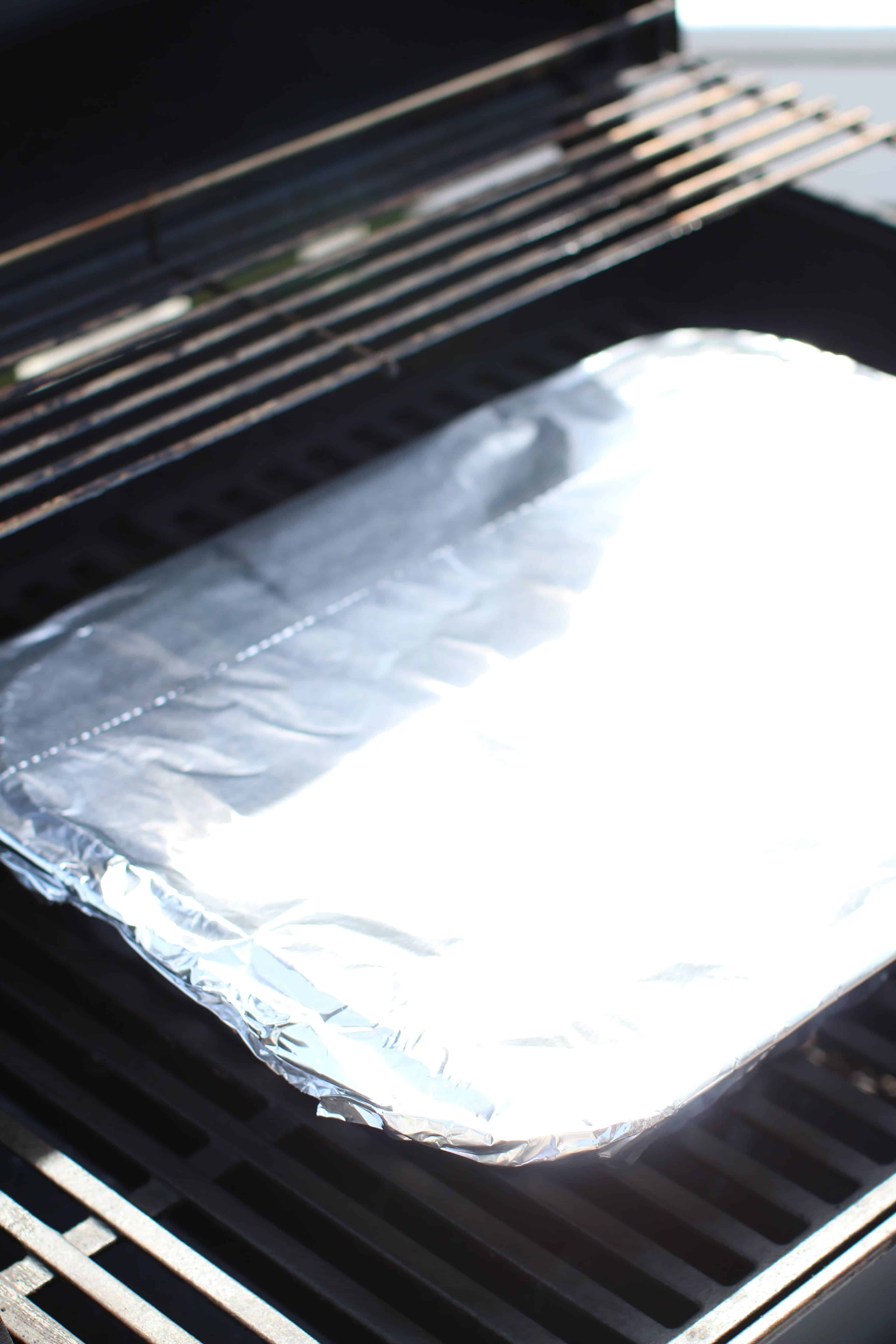 A covered aluminum foil pan on the grate of a gas grill
