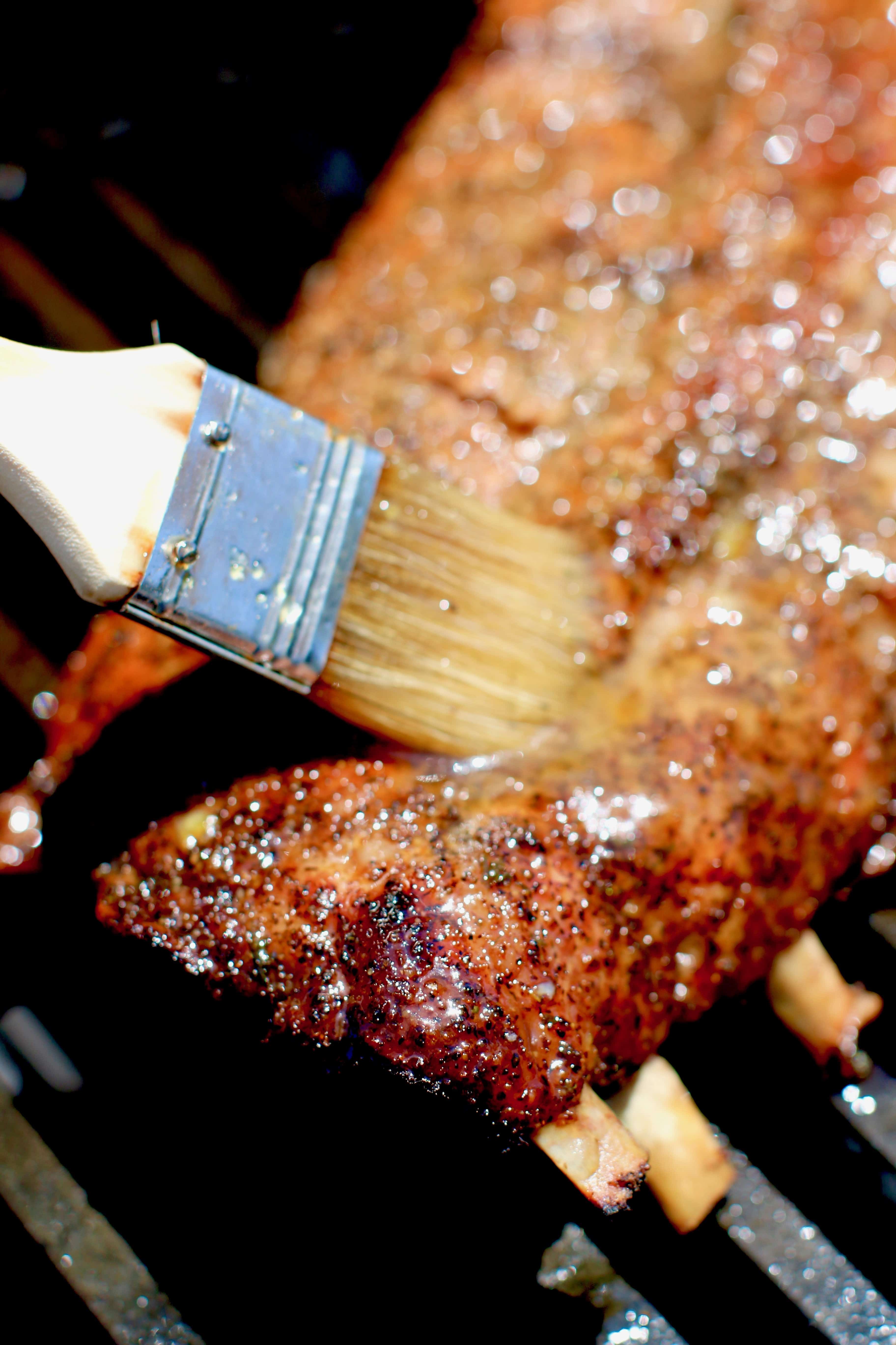 Pork ribs being slathered with glaze on gas grill.