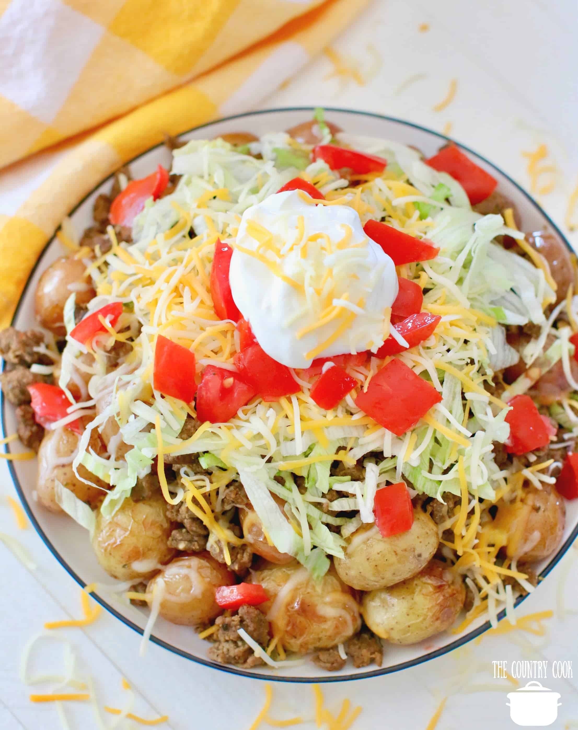 overhead photo of small grilled potatoes topped with taco meat, shredded lettuce, shredded lettuce diced tomatoes and sour cream