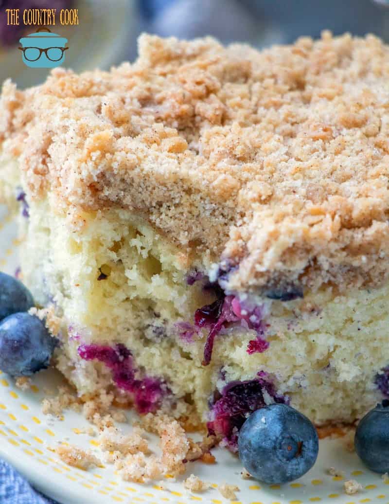Homemade Blueberry Buckle Cake, slice on a plate with fresh blueberries.