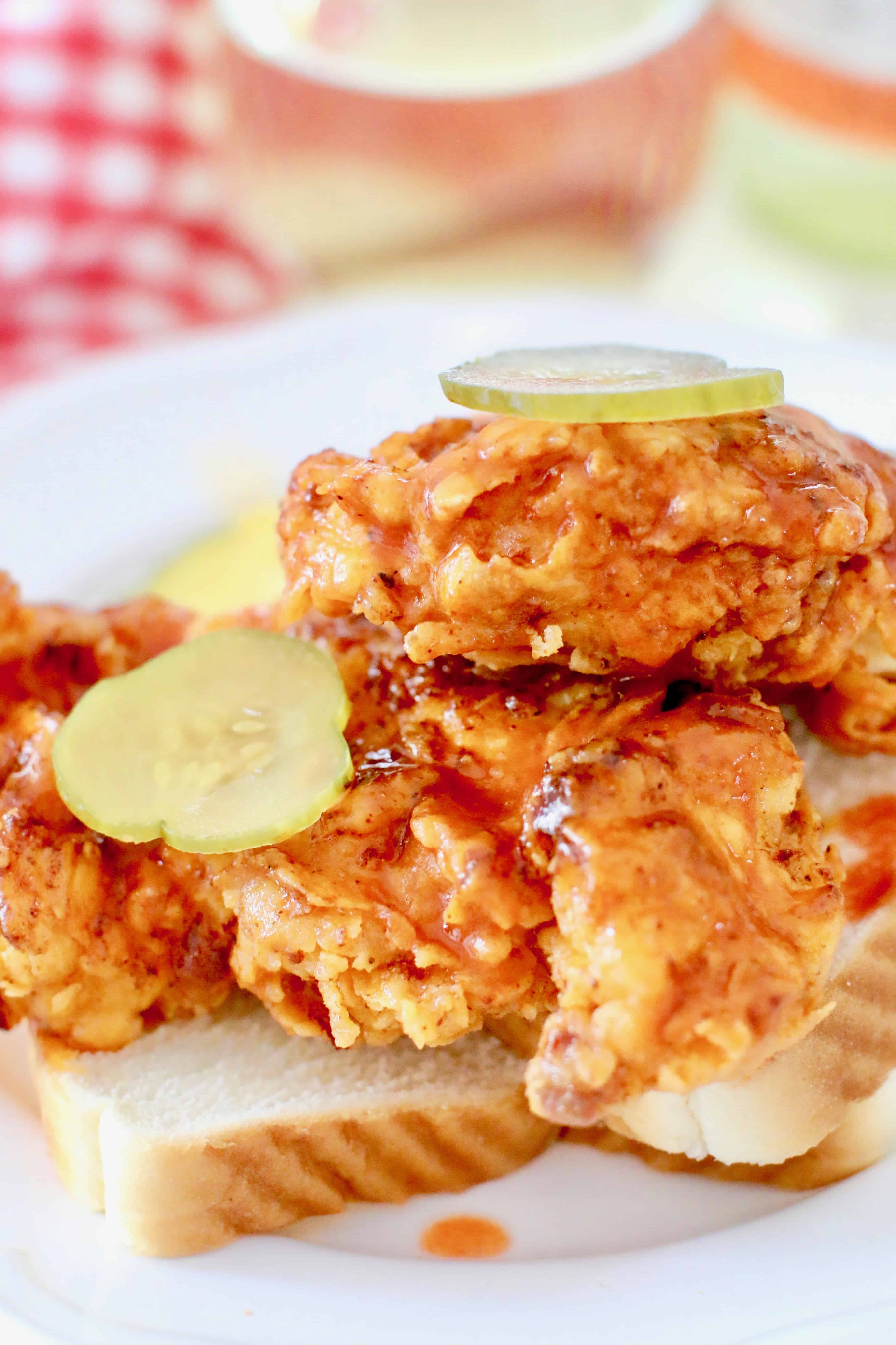 Nashville Fried Hot Chickenpieces on slices of white bread with sliced pickles on top.