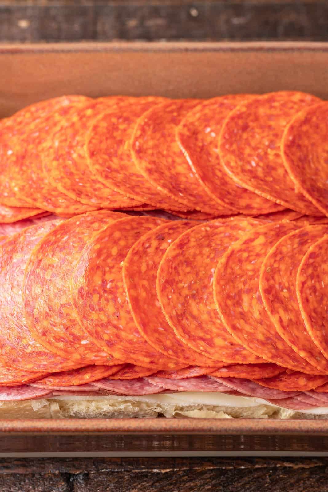even layers of salami and pepperoni on top of a layer of sliced cheese. 