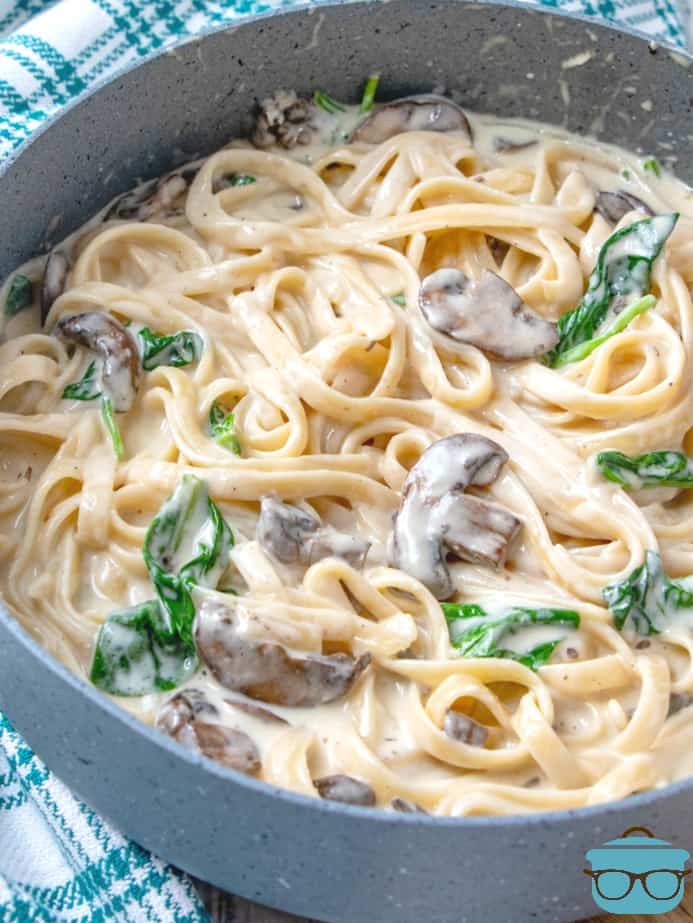 Homemade Creamy Garlic Parmesan Fettuccine Alfredo with fresh spinach and mushrooms in a large skillet.