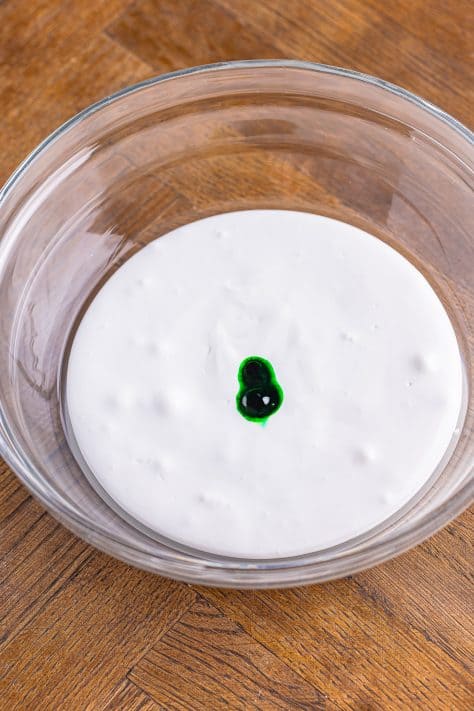 green food coloring added to marshmallow fluff mixture in a bowl.