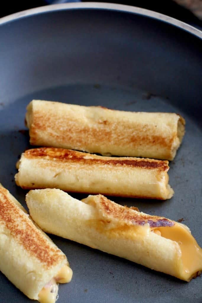 grilled cheese rollups browning in a frying pan.