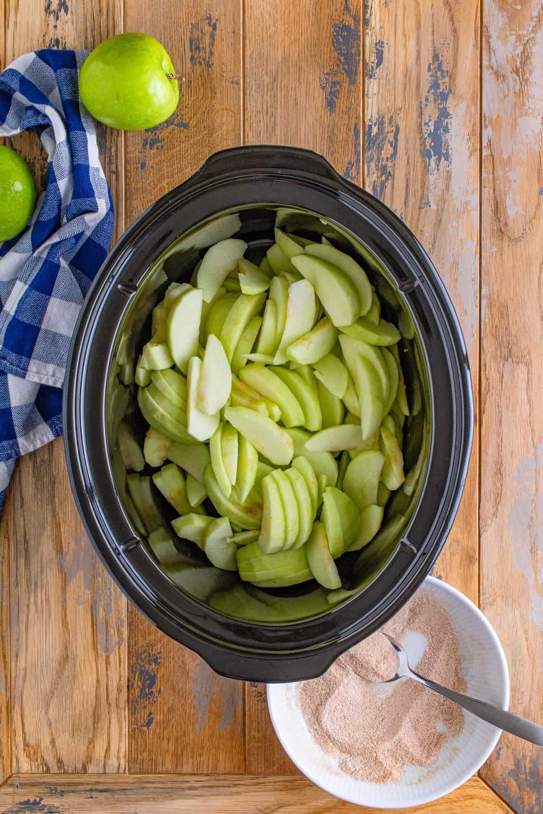 sliced green apples in the bottom of an oval slow cooker.