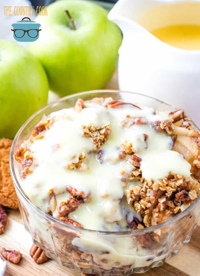 Crock Pot Apple Crisp in a clear bowl topped with an easy warm vanilla sauce.