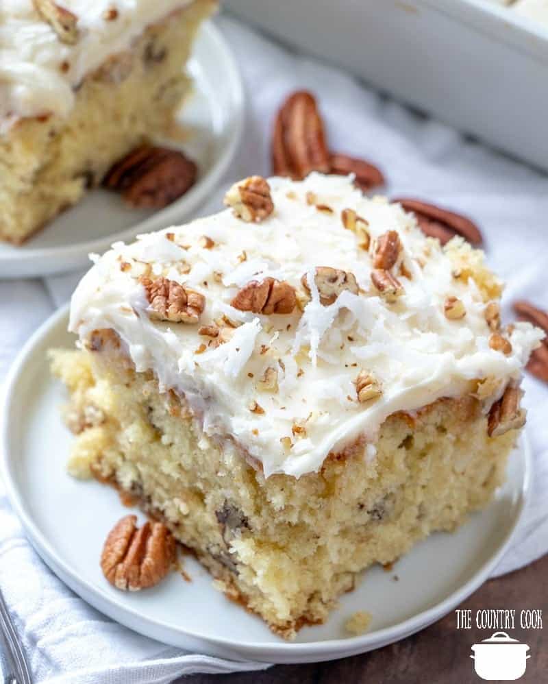 The Best Homemade Italian Cream Cake with Butter Cream Cheese Frosting recipe. Slice shown on a small round white plate with pecans scattered around. 